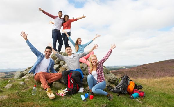 Seks ungdommer poserer smilende med armene opp ute i et naturlandskap