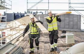 To arbeidere på byggeplass bærer materialer.